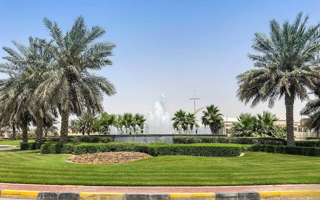 A park in Al Forsan Village featuring palm trees and a central fountain, creating a serene outdoor atmosphere.