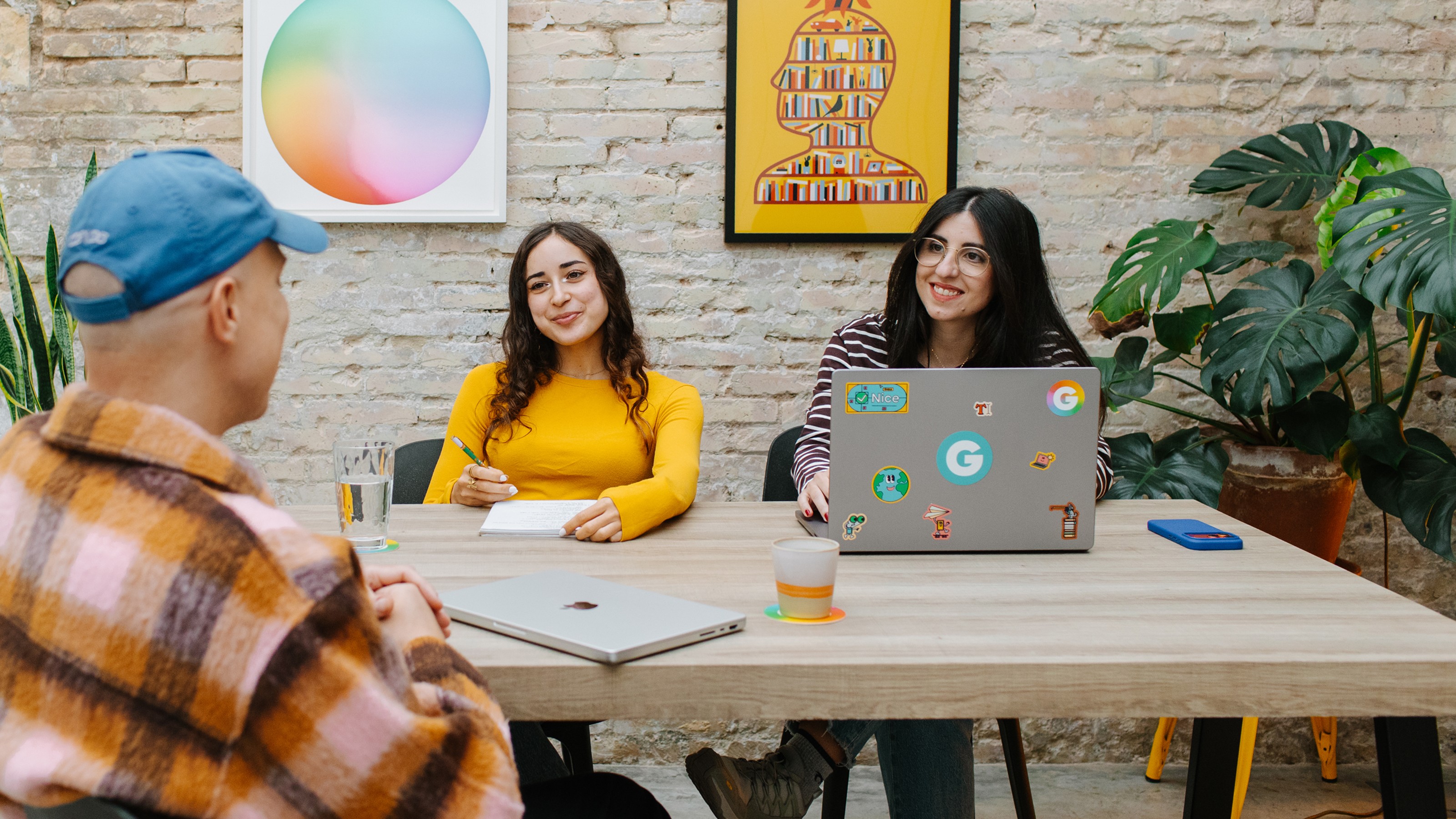 Four people sitting at a table working on their laptops while talking and smiling.