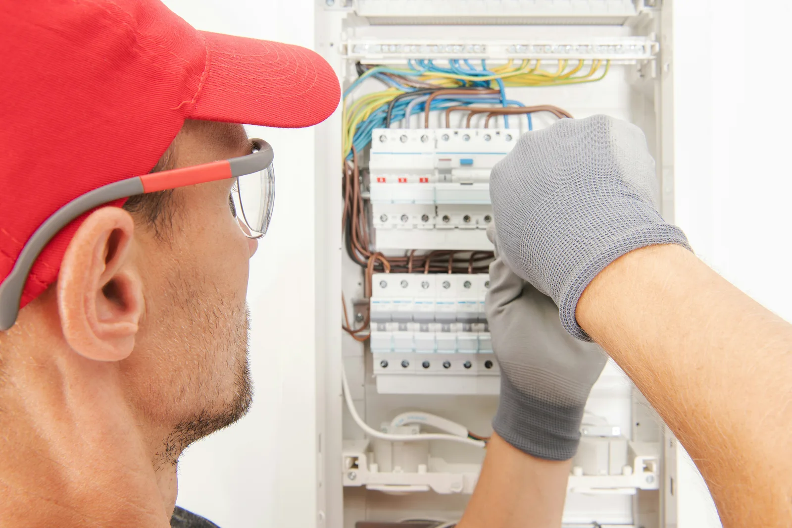 Electrician with red cap inspecting circuit breakers inside distribution board