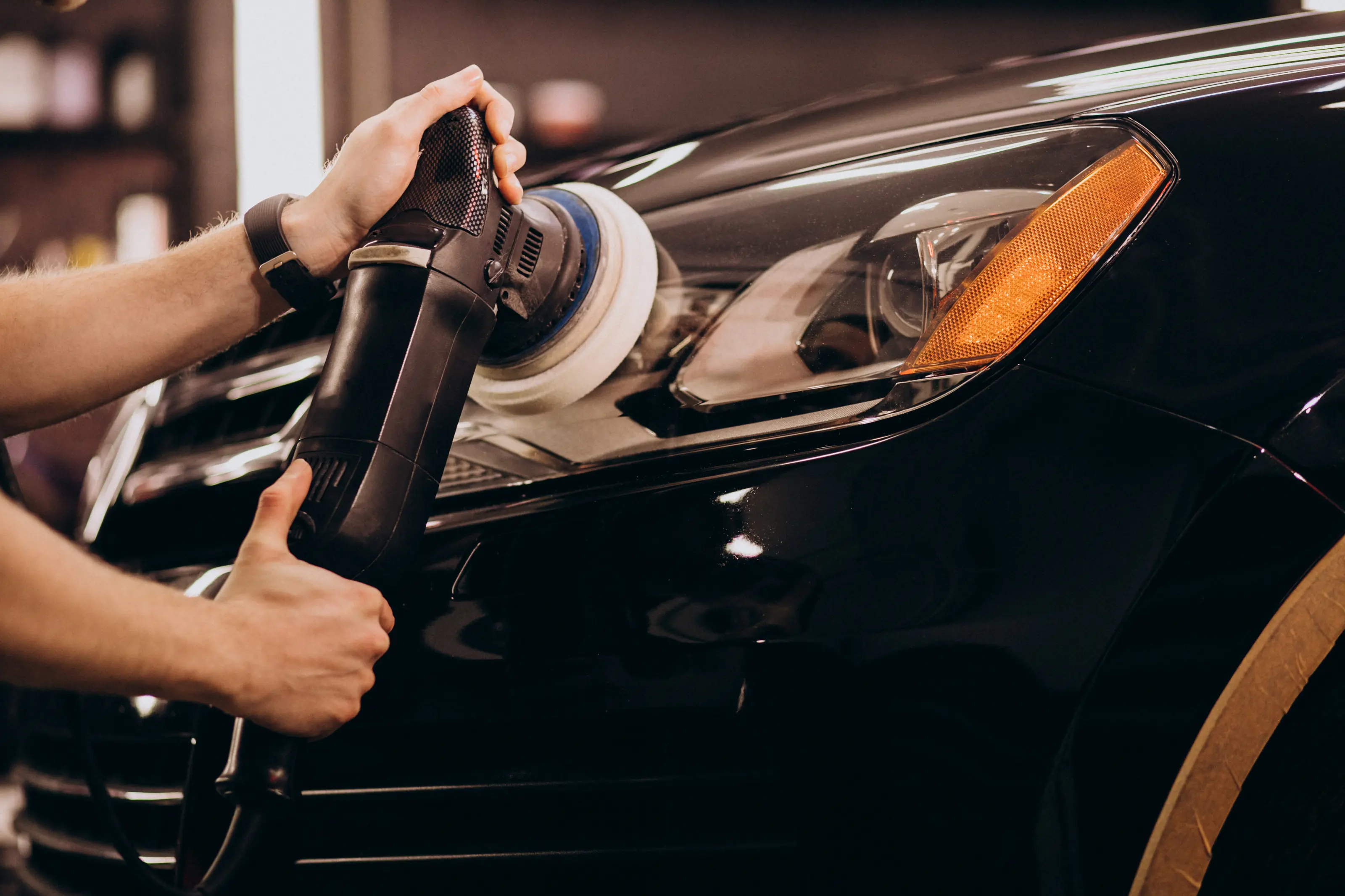 Close-up of a professional detailer in Houston using a dual-action orbital polisher for paint correction and scratch removal on a black luxury car.