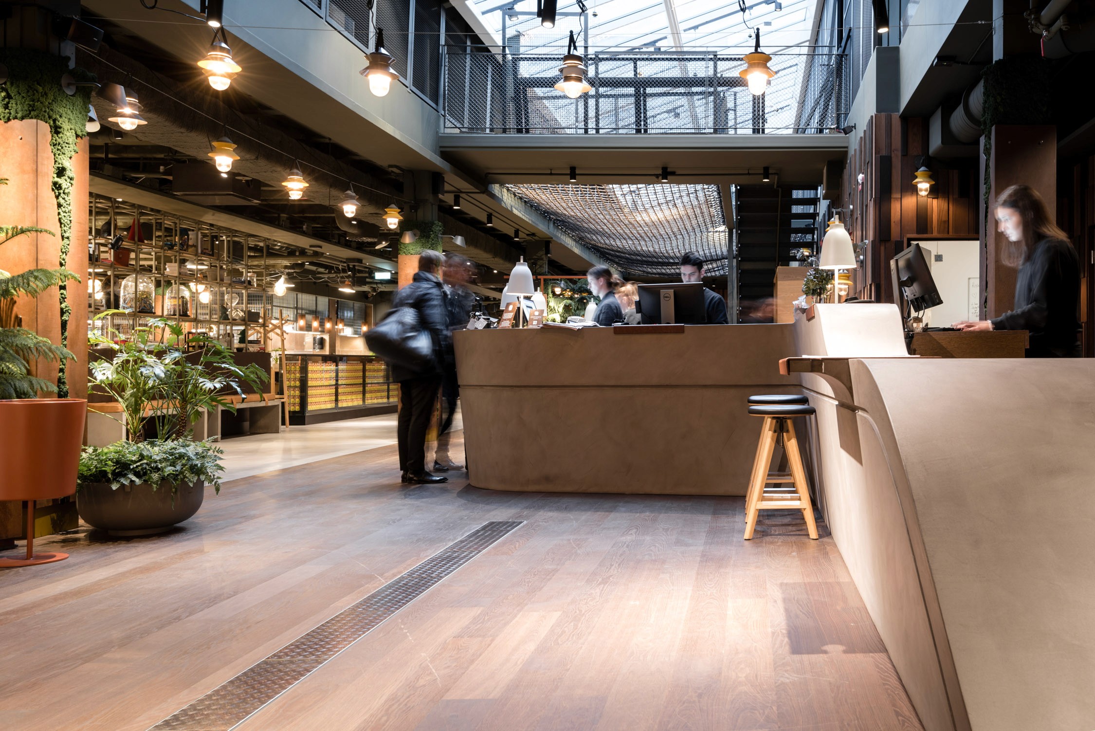 A modern industrial cafe interior with wood floors, hanging Edison bulbs, a long counter, and patrons seated at tables.