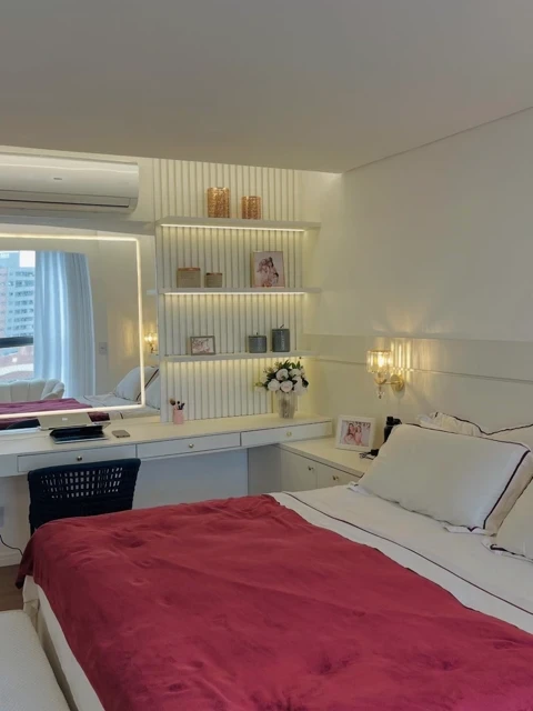 A cozy bedroom with a large glass window offers a stunning mountain view, featuring shelves filled with books and a white bed.