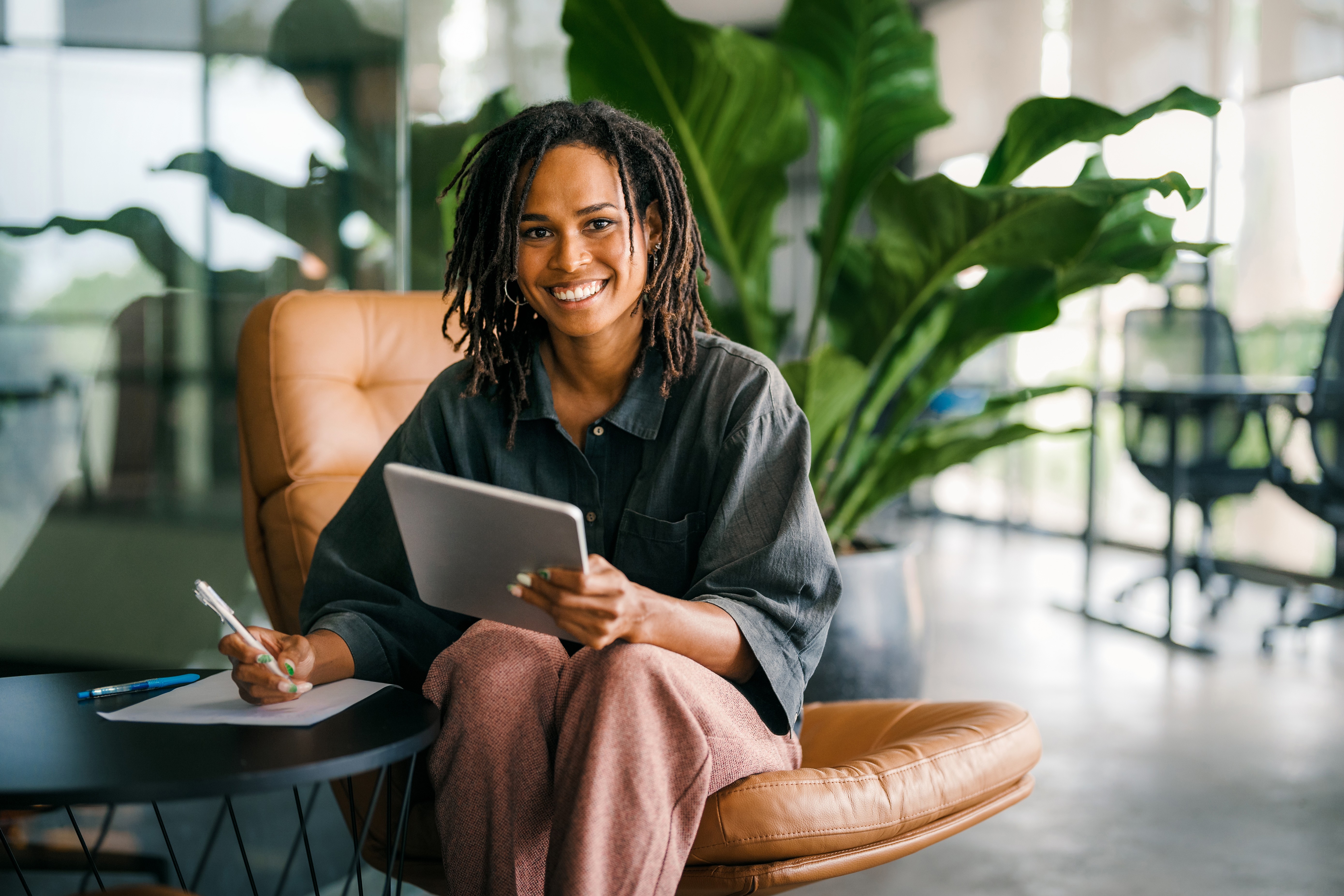 Woman smiling while sitting in a lounge chair, writing notes with a tablet