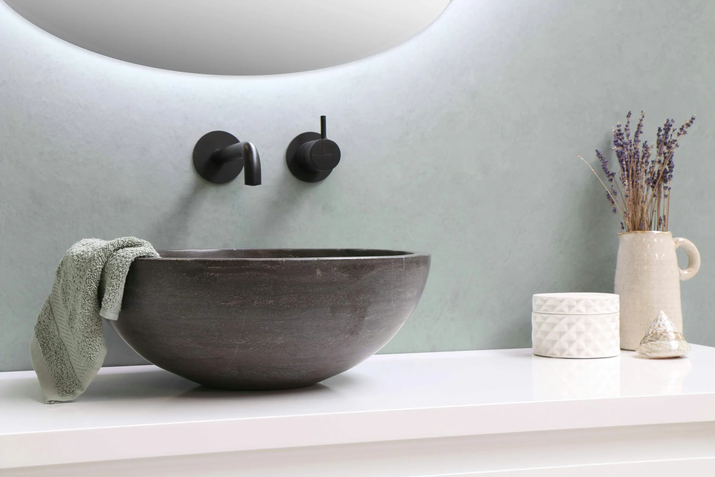 Dark stone vessel sink with a wall-mounted faucet in a modern bathroom