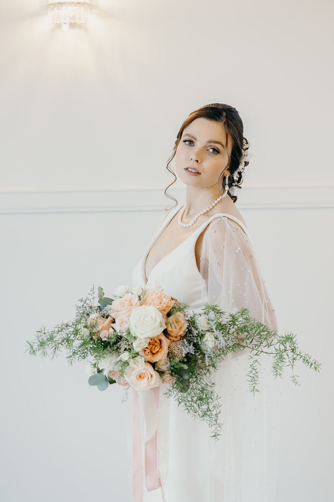 Bride with romantic peach and white bouquet featuring greenery and roses by Des Moines Iowa florist.