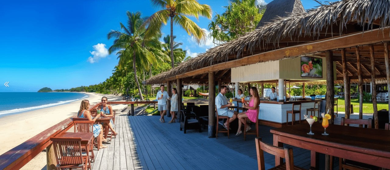 Couples enjoy drinks and sunshine along the deck of the beachside bar at Uprising Resort in Fiji