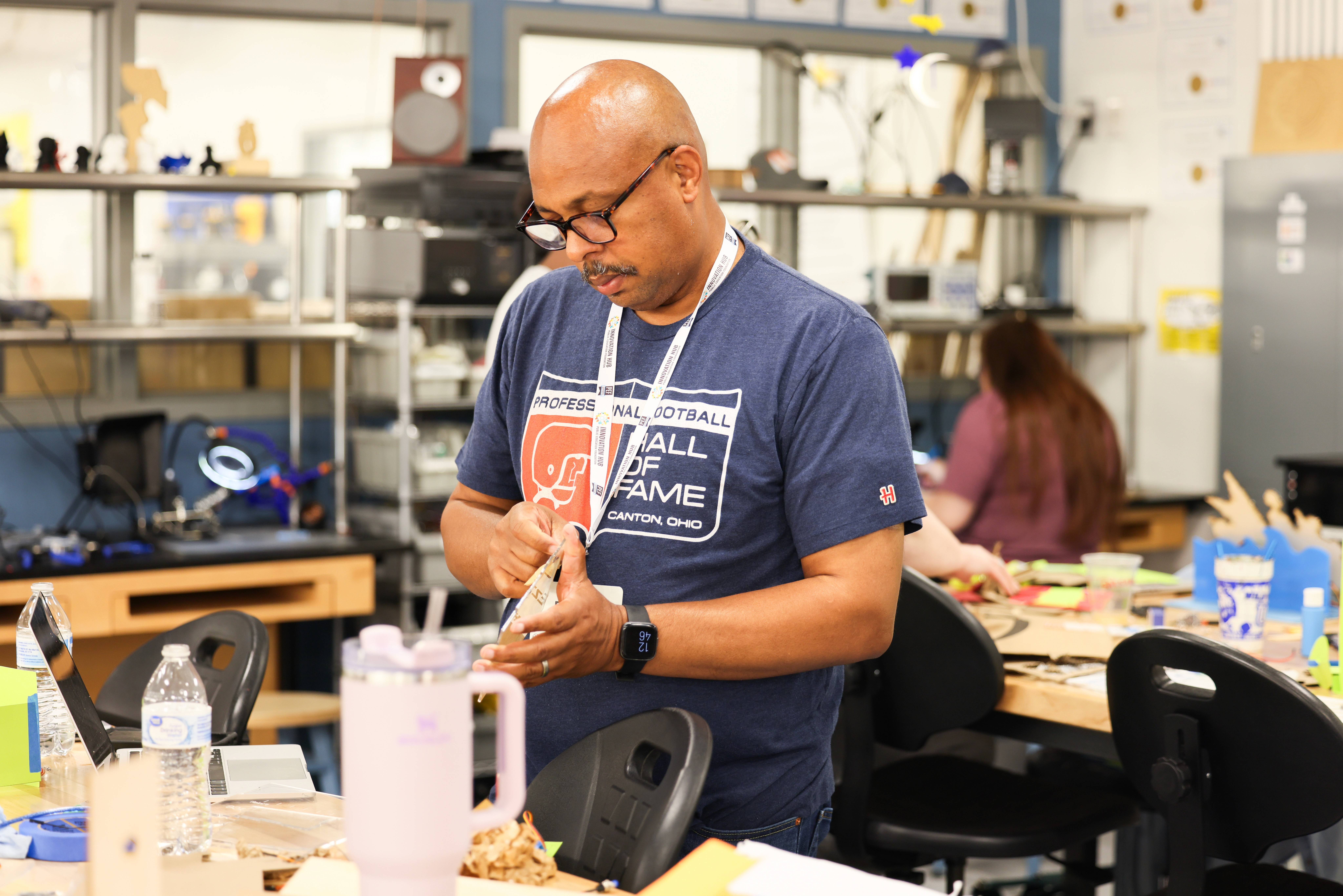 A teacher standing up in a fabrication lab working on a hands on project. 