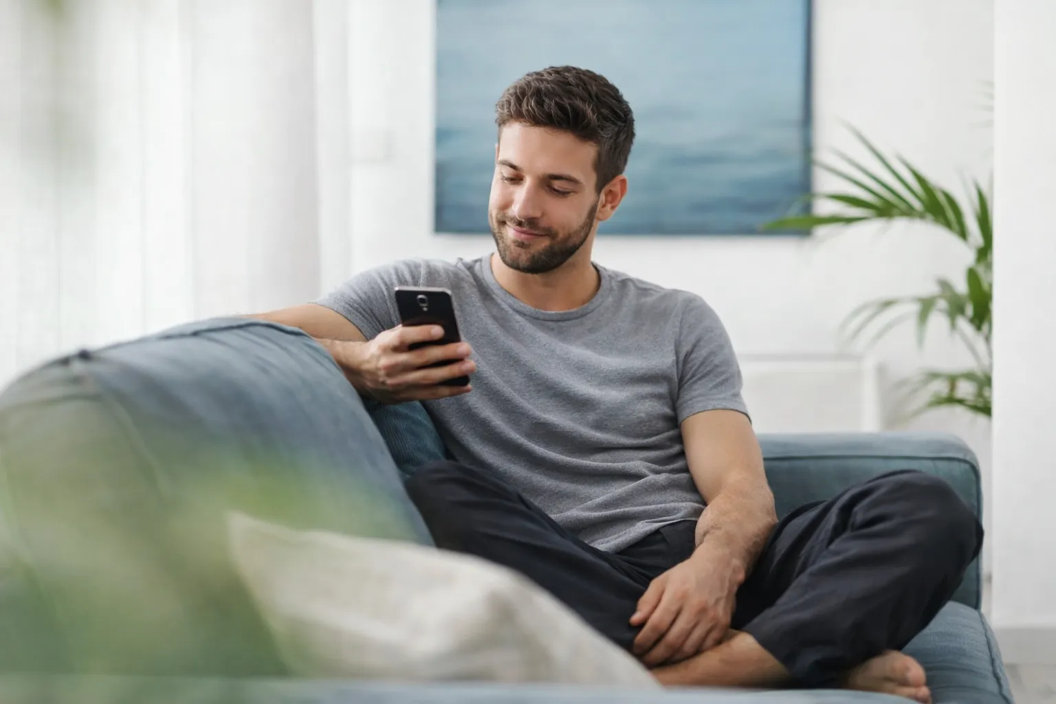 Neura Health Man sitting on a couch in a bright living room looking at his smartphone.