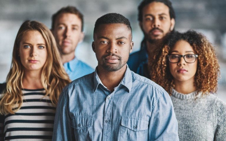 A diverse group of five colleagues standing together in a professional setting, looking at the camera