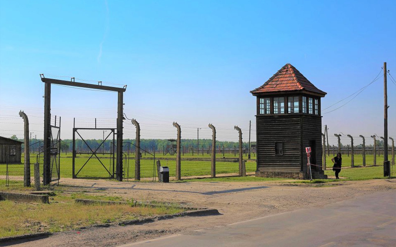 Auschwitz-Birkenau inngangsport og vakttårn undir heiðskíru himni.