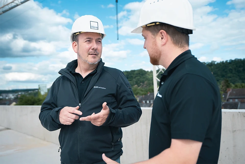 Zwei Mitarbeitende von Fries Architekten tauschen sich auf einer Baustelle über den Fortschritt eines Bauprojekts aus.