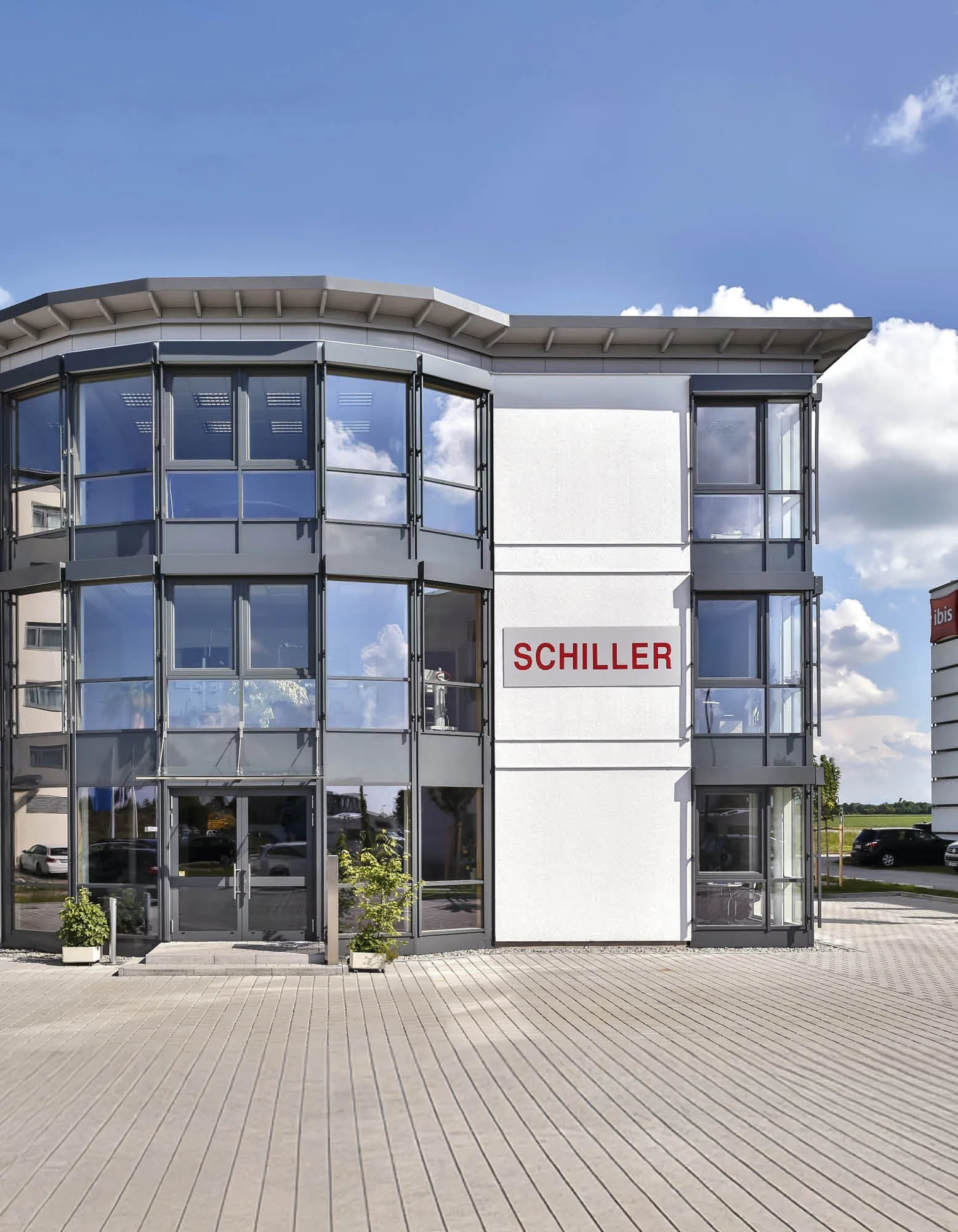 Moderne Geschäftsgebäude mit Glasfront und dem Schriftzug "SCHILLER" auf weißer Fassade, bei strahlend blauem Himmel.
