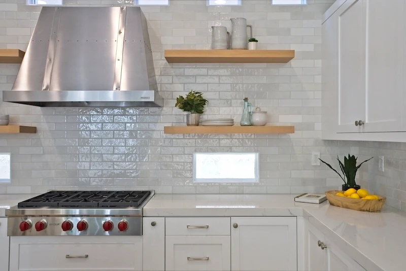 Detailed kitchen range area with stainless hood, floating shelves, and glossy subway tile in Bonita Canyon Remodel.