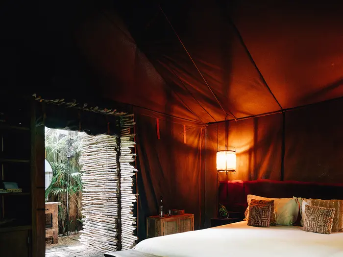 Deluxe Tent at Nômade Tulum featuring spacious bed with pillows and cushions, and a beautiful lamp lighting the room.