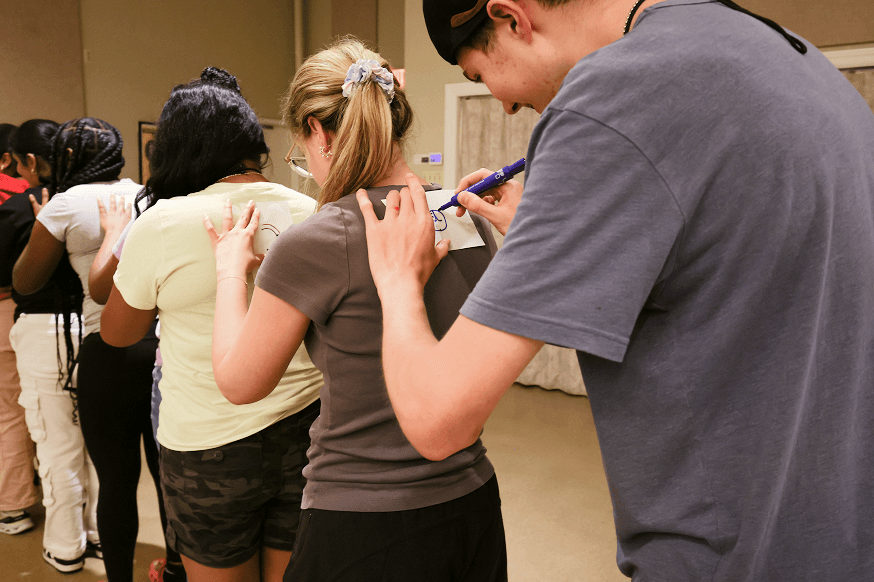 Students participating in a group activity, writing notes on each other’s backs, representing youth engagement and community-building programs.