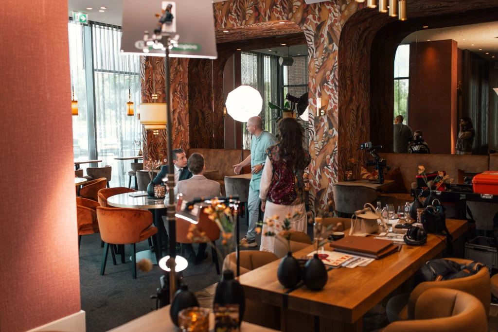Een gezellig en elegant ontworpen restaurantinterieur toont een groep mensen in gesprek rond een tafel, omringd door warme verlichting, moderne decoratie en luxe zitplaatsen, wat een verfijnde eetervaring creëert.