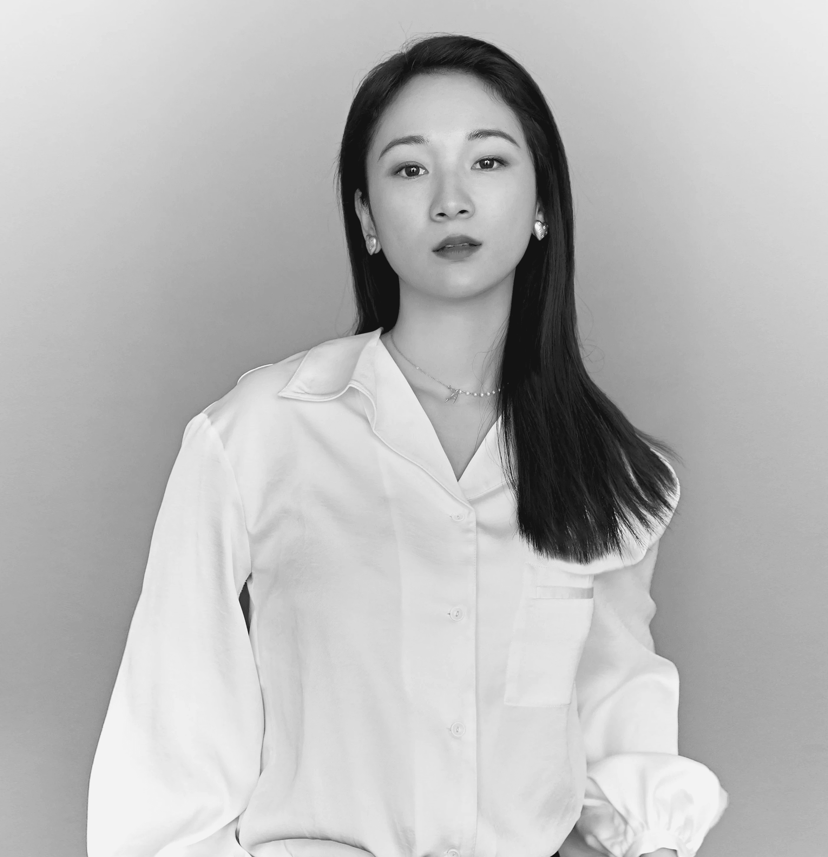 A thoughtful young person with dark hair gazes to the side, captured in soft black and white lighting.