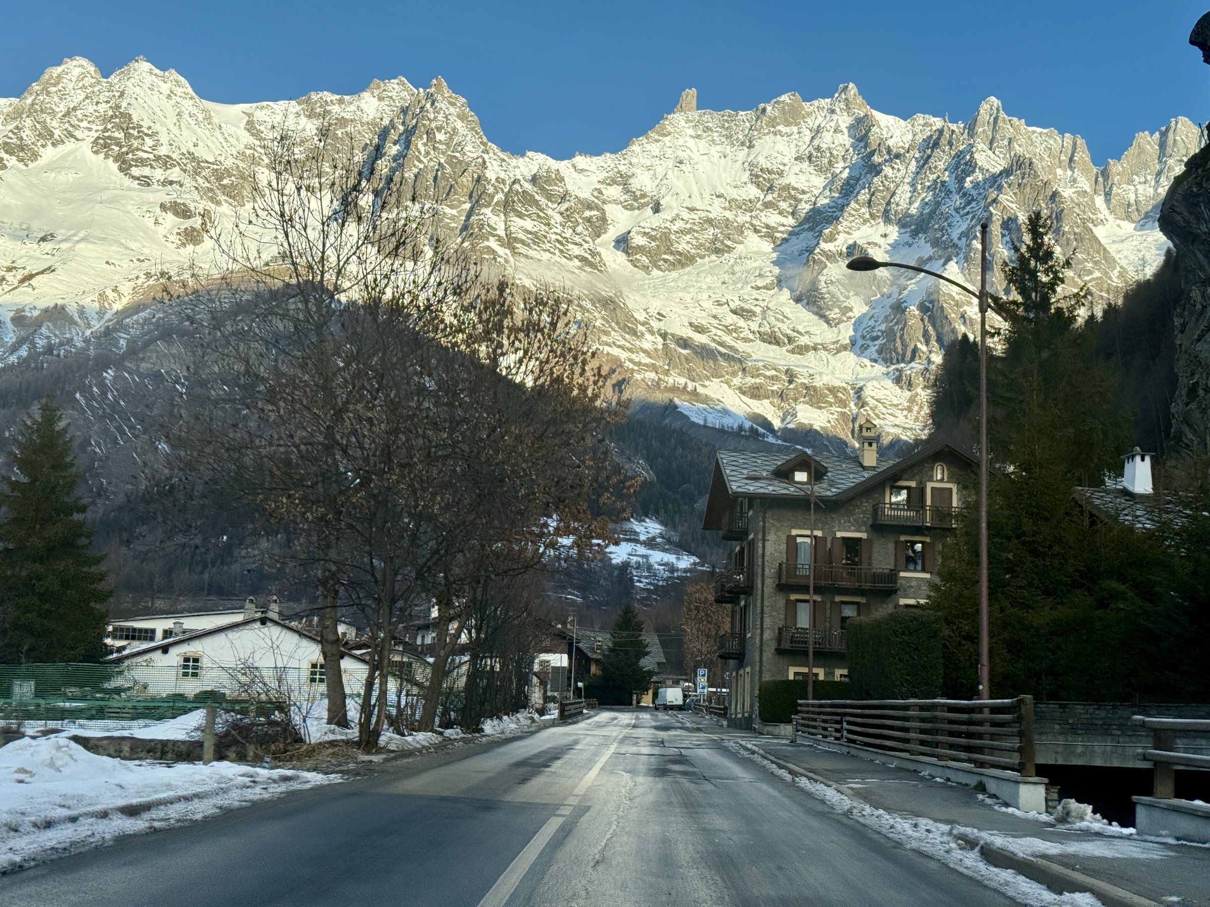 Village road with stone chalet leading toward the sunlit snowy Mont Blanc massif near Courmayeur, Italian Alps