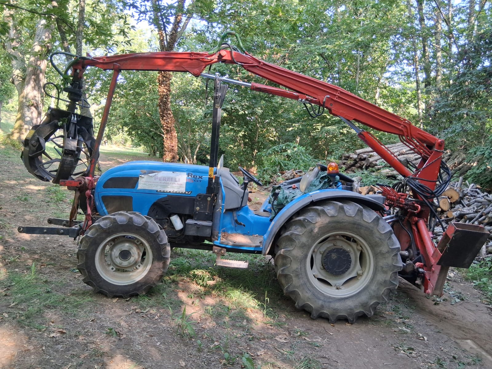 Trattore compatto con braccio per movimentazione e recupero di legname in area boschiva