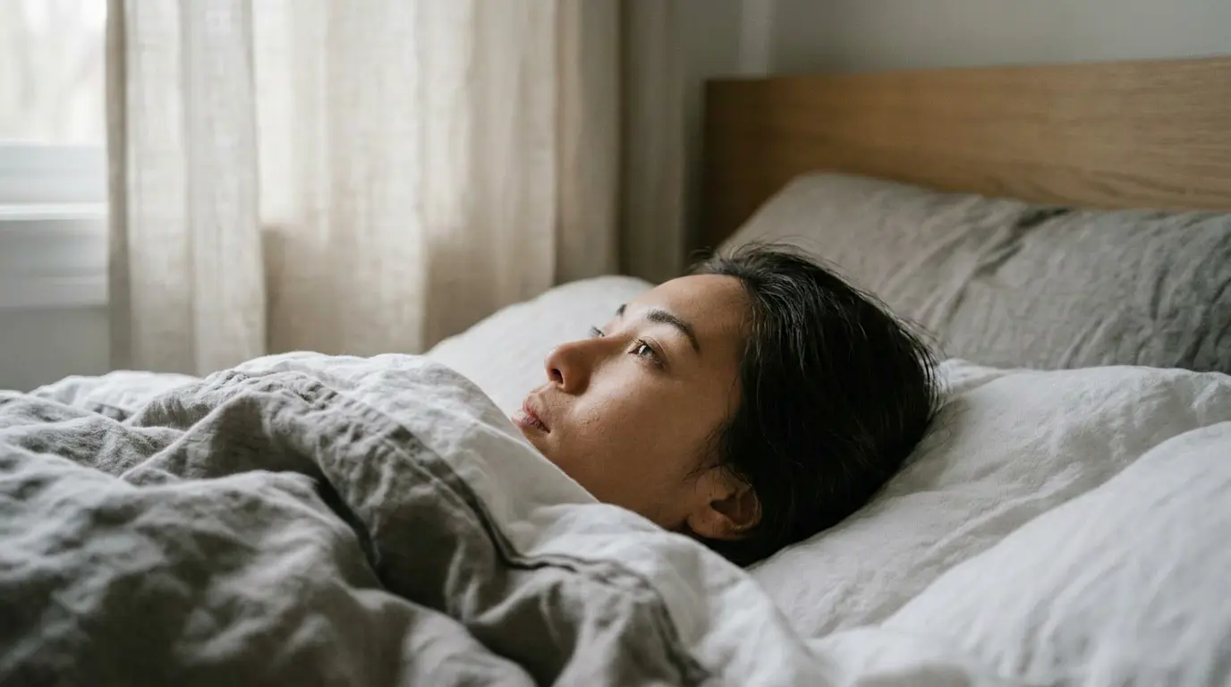 Person lying awake in bed looking toward a window in soft morning light