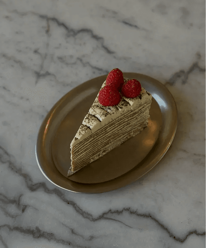 A slice of matcha (green tea) layered cake topped with fresh raspberries, served on a gold-rimmed plate against a marble surface