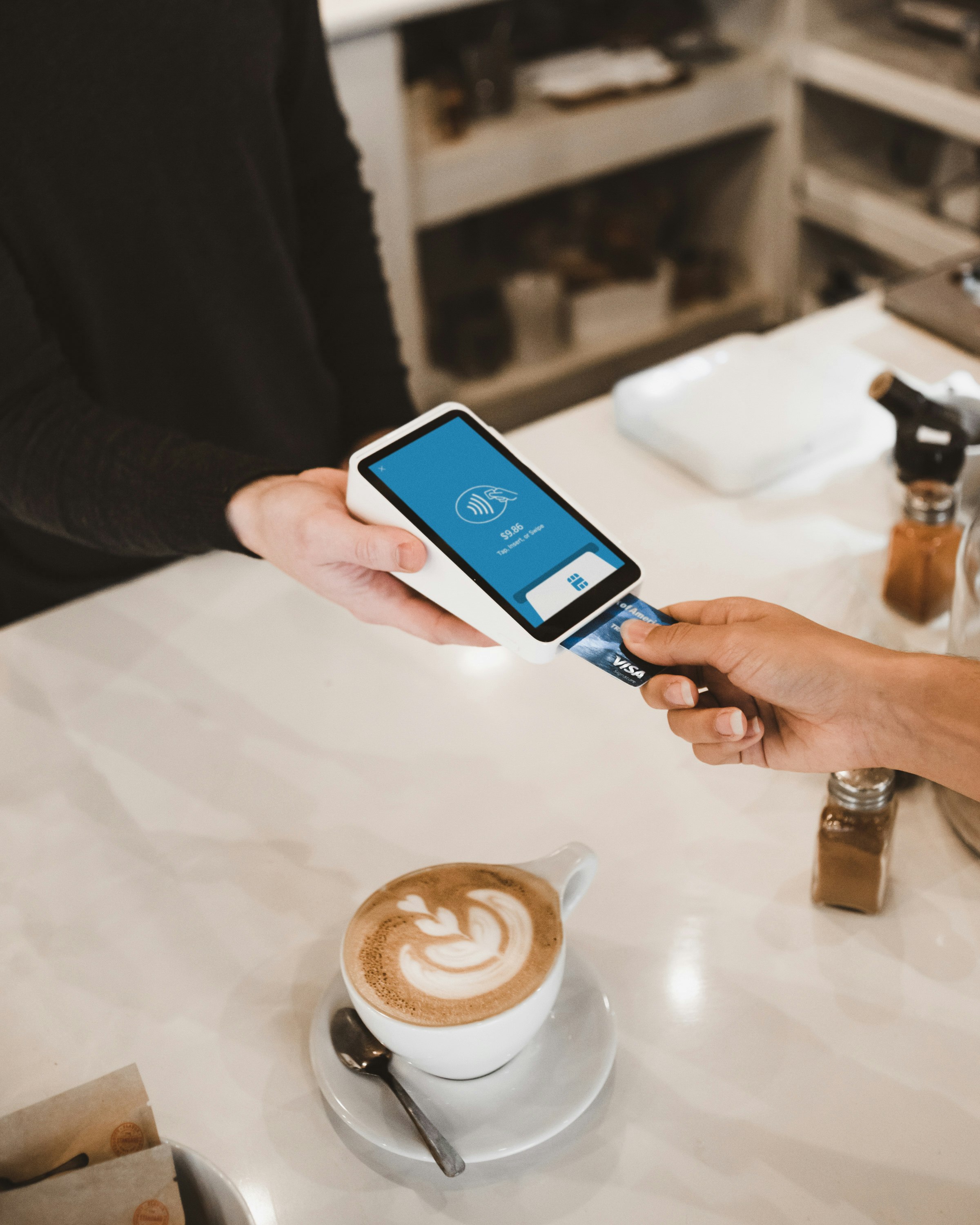 Eine Person zahlt mit Visa-Karte am Kartenterminal eines Cafés – der einzige Zahlungsweg, von dem viele Händler abhängen.