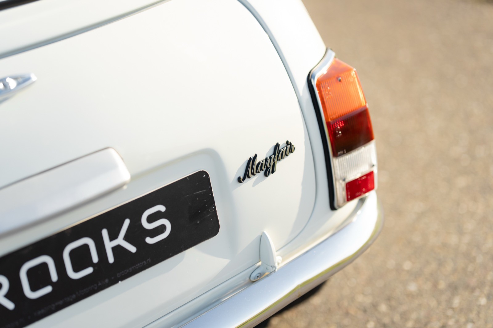 Close-up of a white vintage car's rear, showcasing the taillight and license plate that reads "BROOKS."