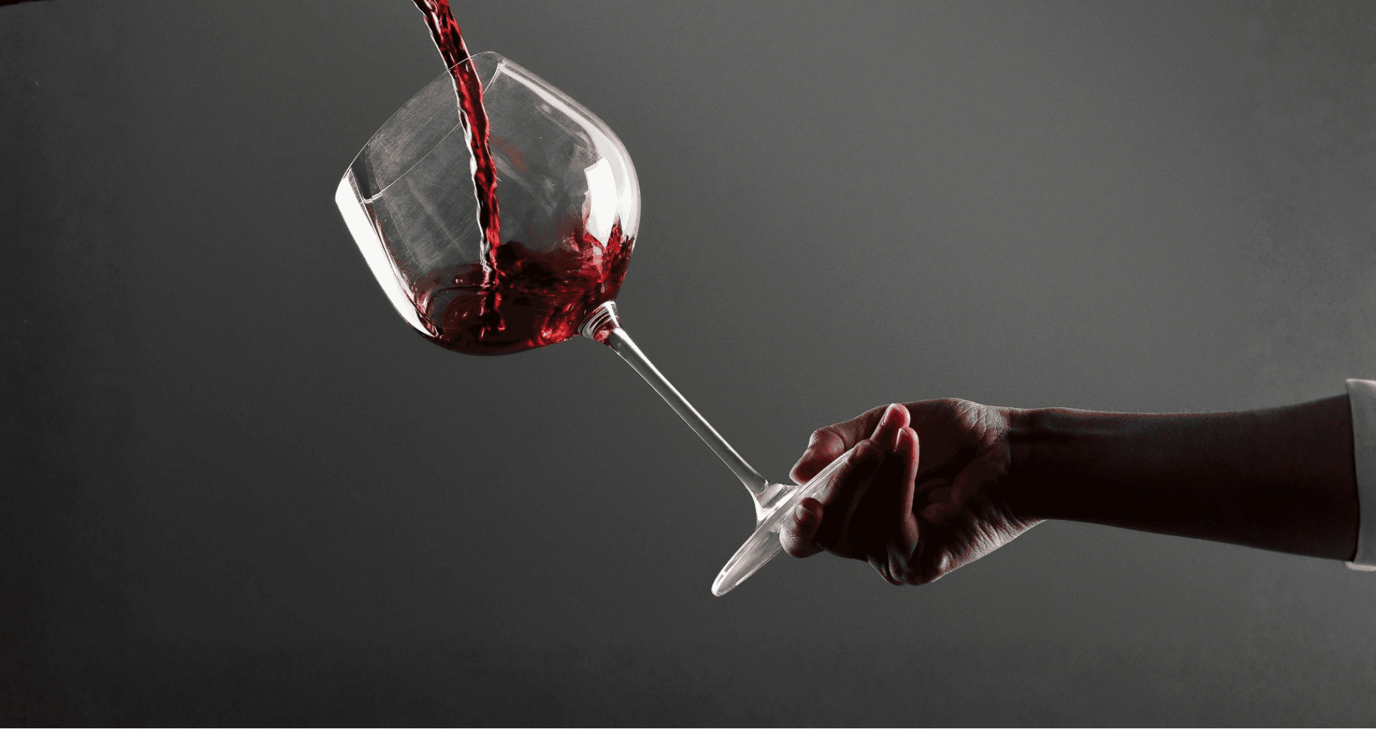 Photo d'un bras tenant un verre de vin dans lequel coule du rouge