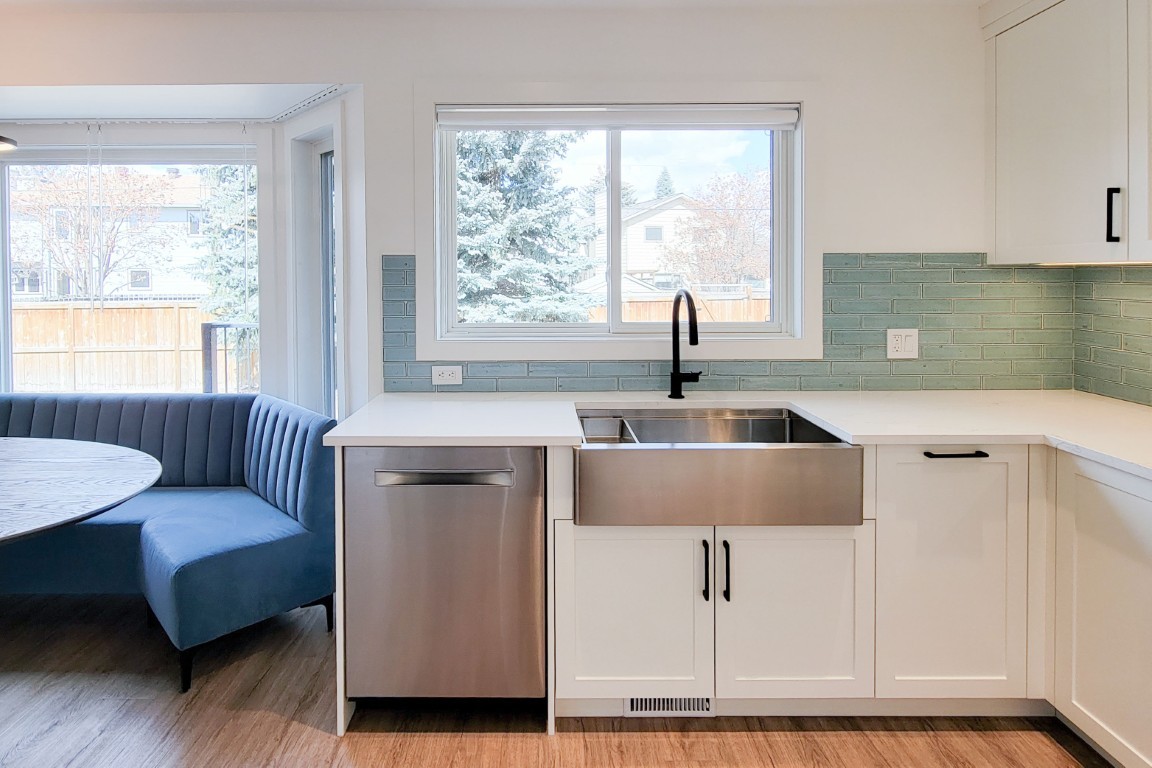 Image of KHD Homes kitchen design with white cabinets, stainless steel sink, and blue accent seating area.