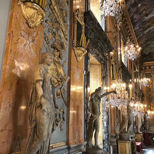 대리석 기둥, 화려한 조각상, 크리스탈 샹들리에, 그리고 벽과 천장의 금 장식이 있는 고급스러운 홀입니다.