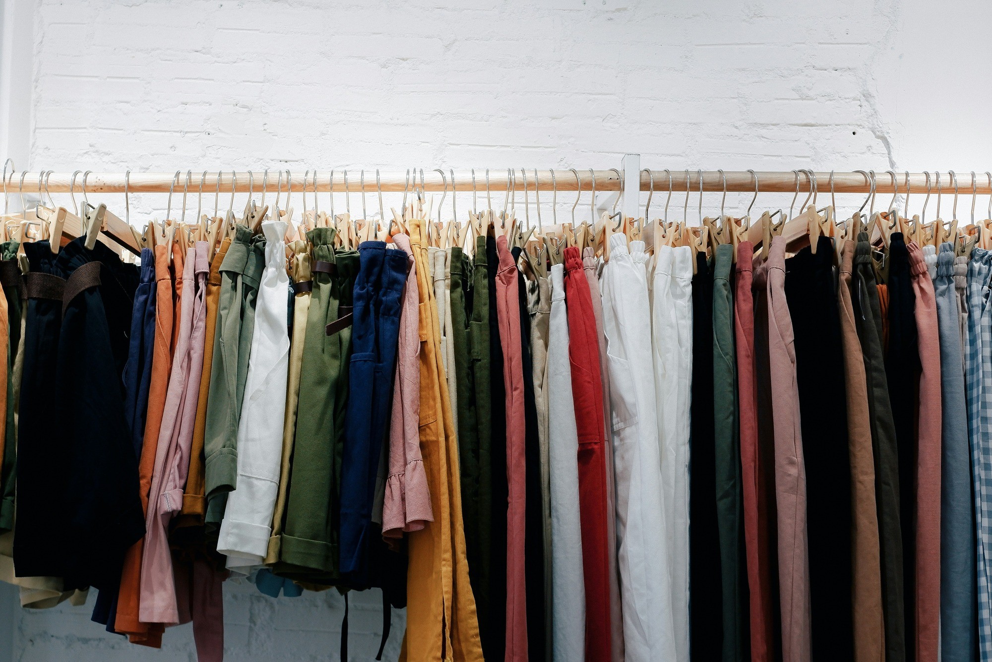 A row of assorted clothing items hanging on a wooden rack against a white wall.