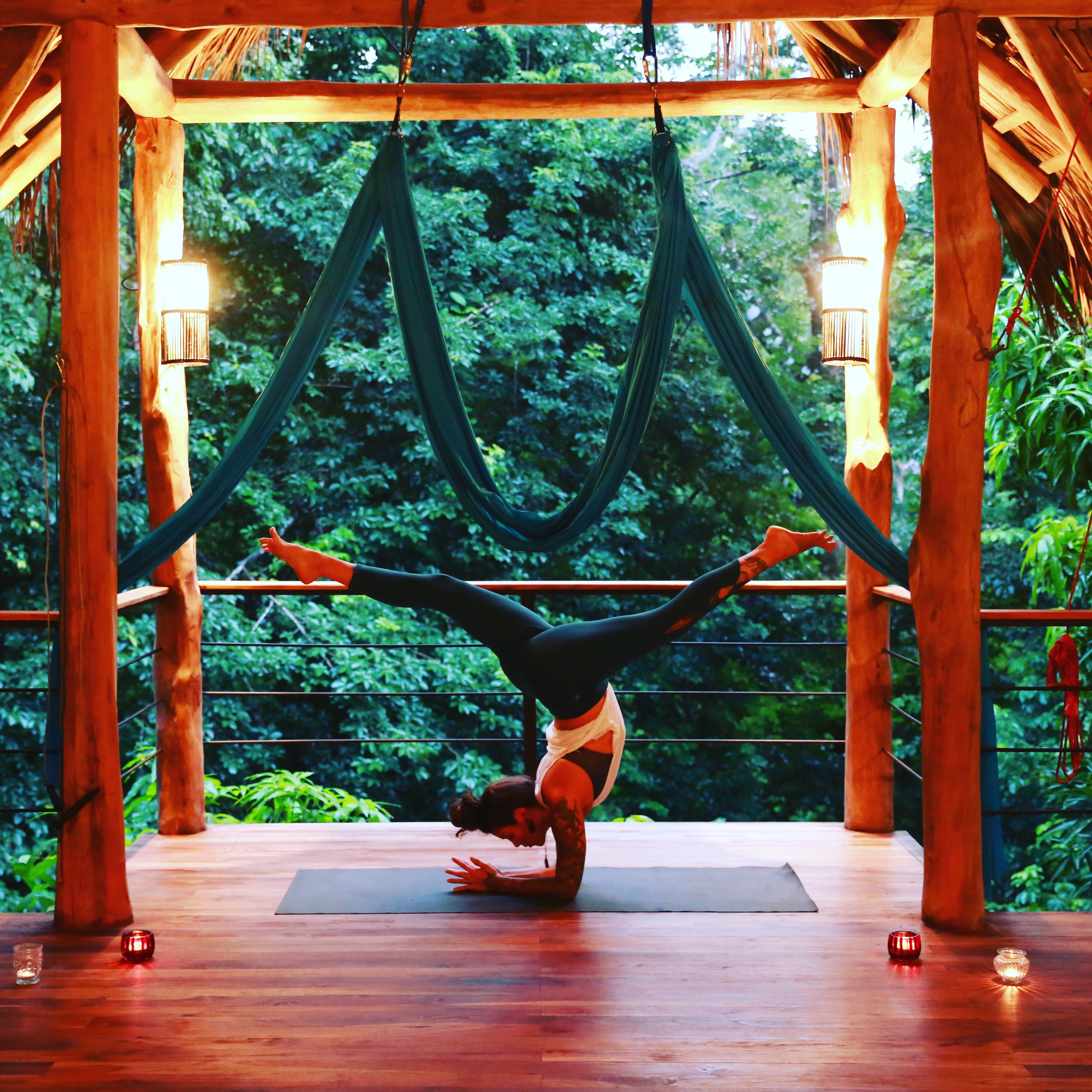 Aerial yoga pose on wooden deck in jungle setting.