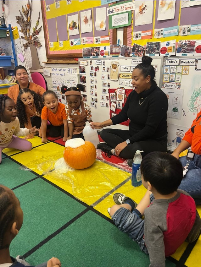 Students look on in amazement as a teacher uses vinegar to create a pumpkin volcano in the classroom.
