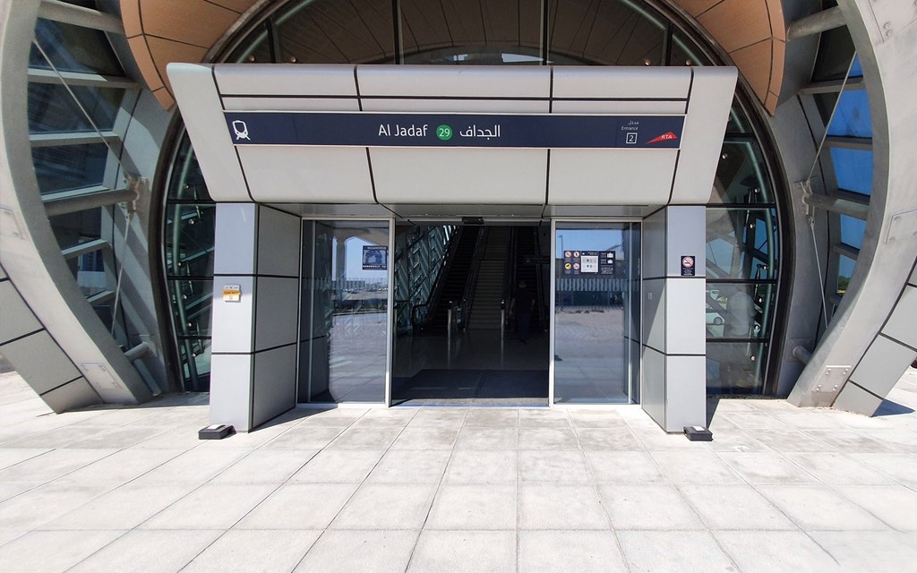 Al Jaddaf Metro Station entrance with curved glass design, RTA signage, and escalators visible inside.