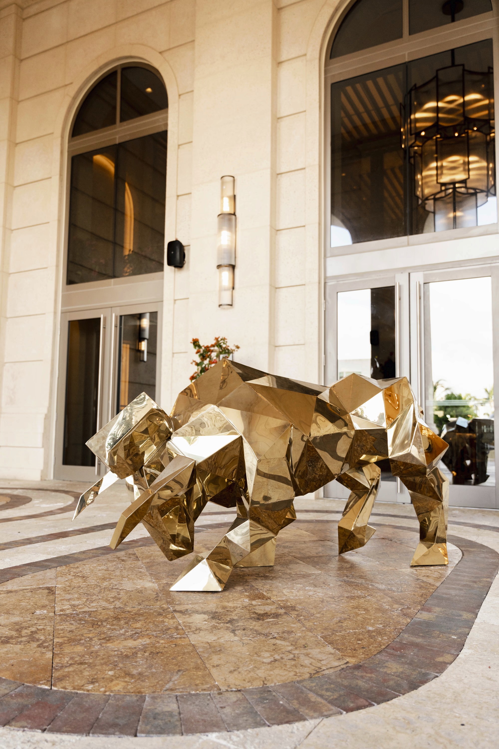 A golden lion sculpture sits outside an entrance, surrounded by stone flooring and large glass doors.