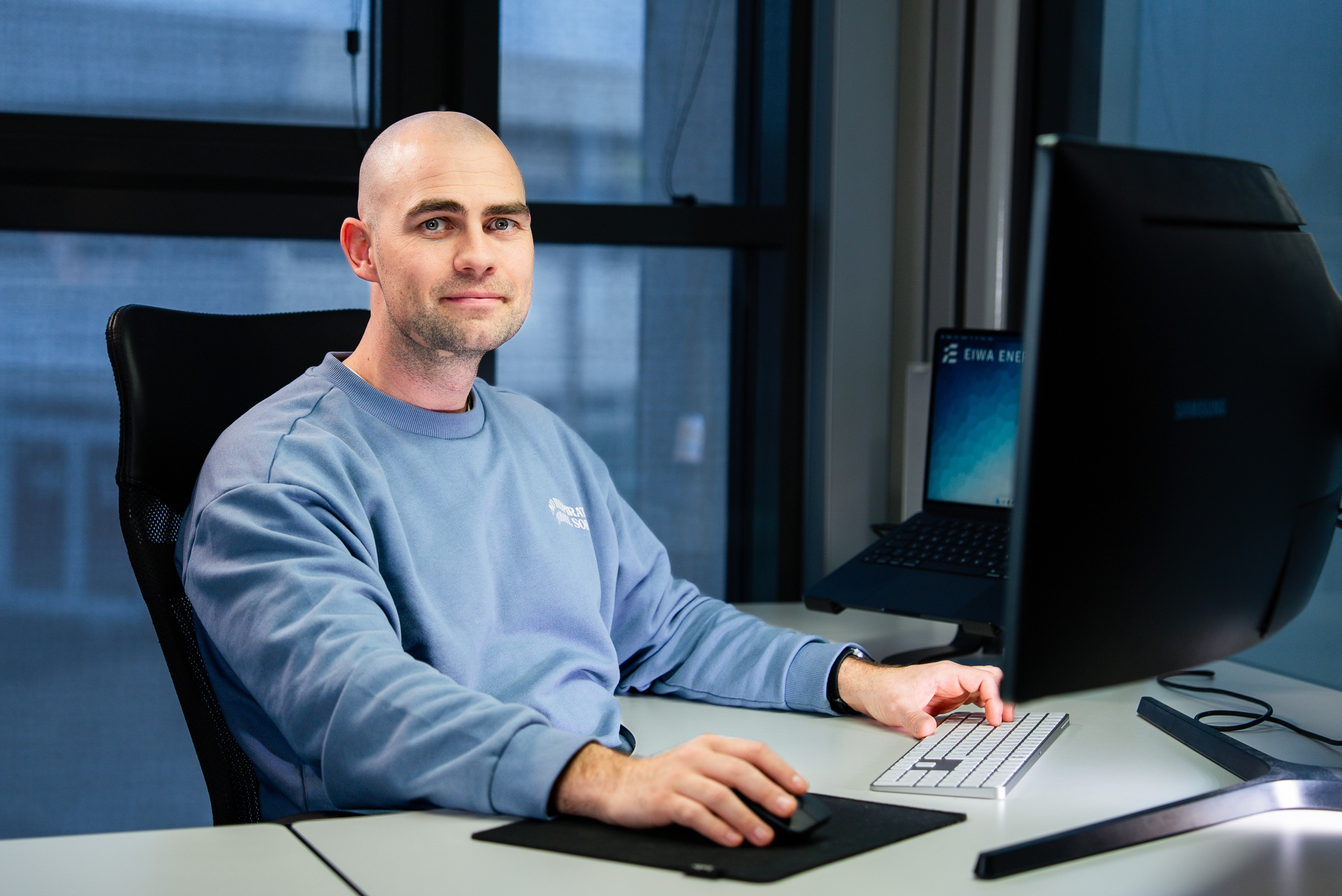 Smiling woman with curly hair and glasses using a smartphone in an office setting.