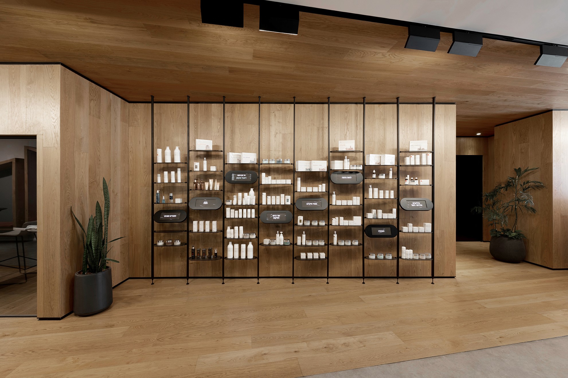 תצוגה קמעונאית יוקרתית: מערכת מדפים מודולרית ממתכת שחורה על רקע חיפוי עץ מלא, המדגישה את מוצרי הפרימיום ומאפשרת גמישות בסידור.