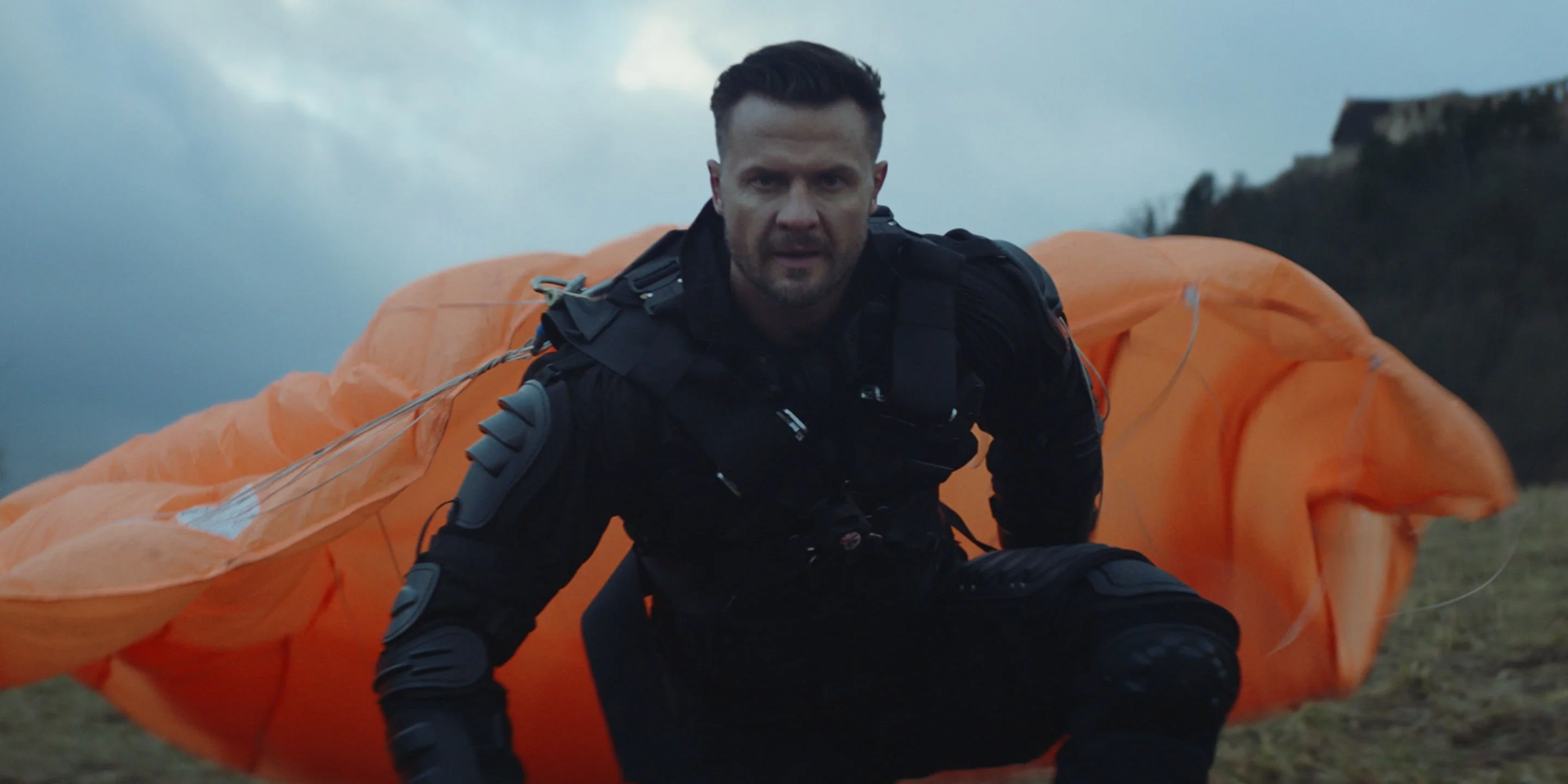 Man in black protective gear crouching in front of a collapsed orange parachute, from the iSelect 'Better Value' campaign