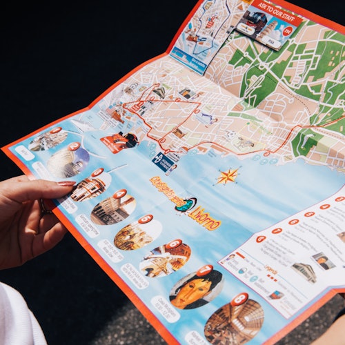 A person holding an open colorful tourist map, showcasing landmarks and attractions of a city.