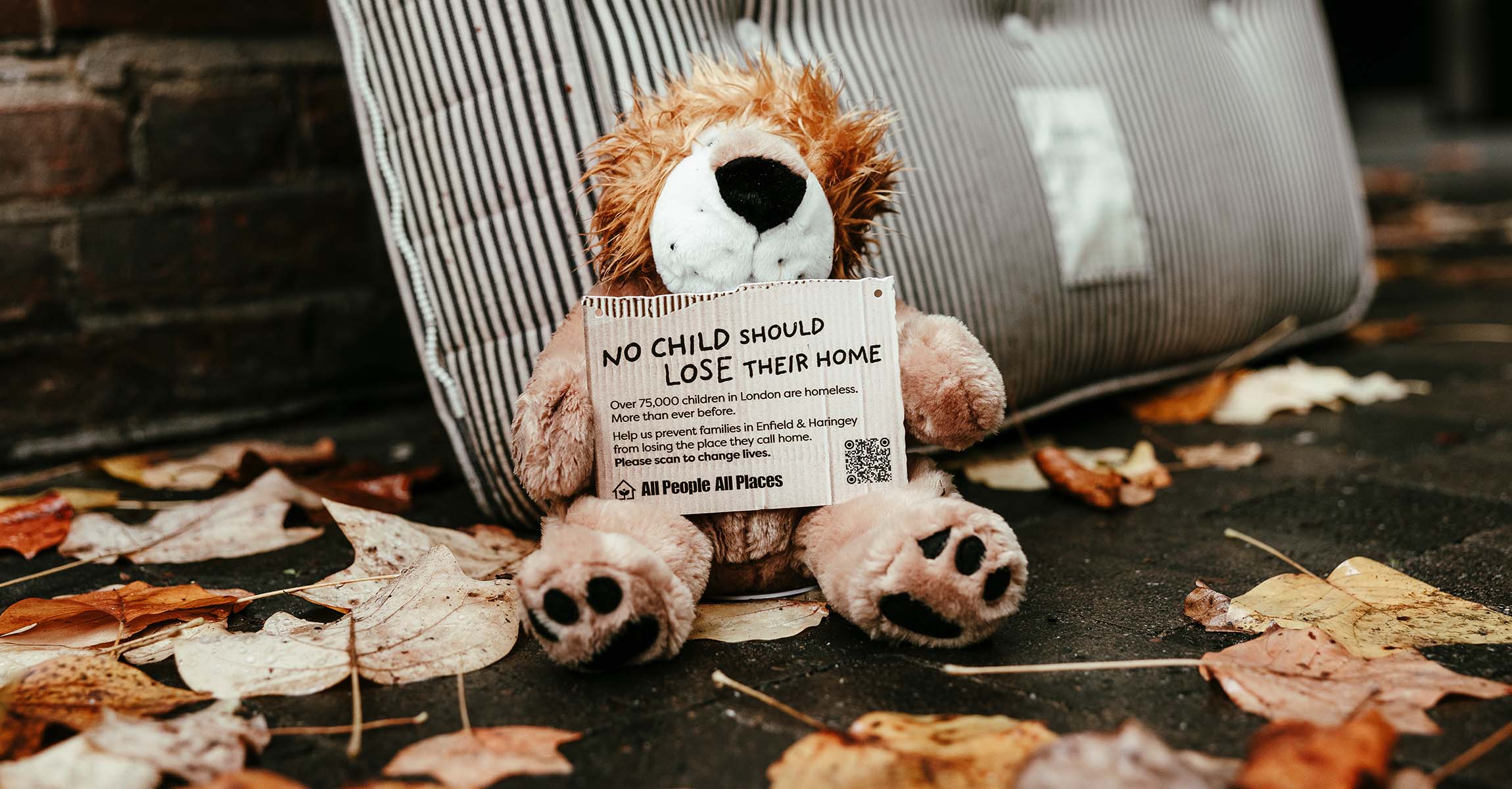 Stuffed Lion toy on a wet pavement holding a sign that says No Child should loose their home
