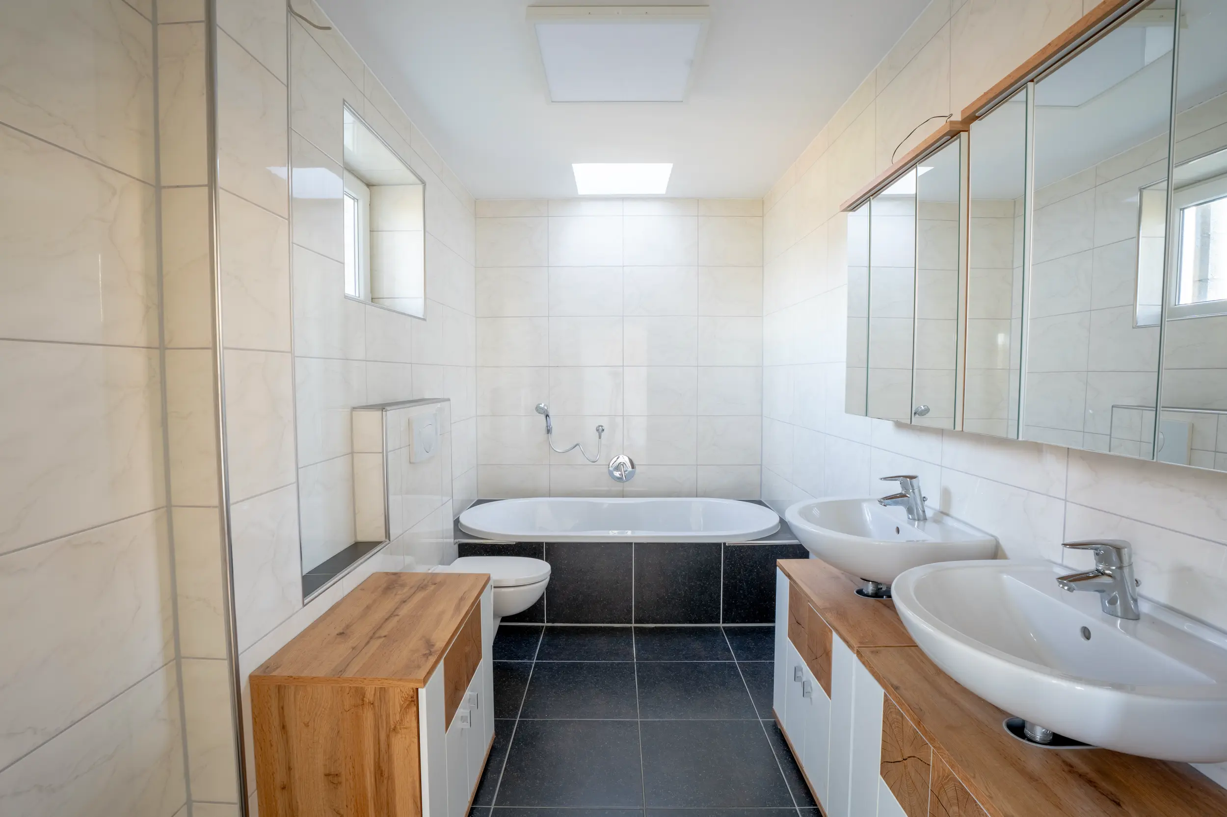 Modernes Badezimmer mit Einbau-Badewanne, Doppelwaschbecken auf Holz-Waschtischen, Spiegelschrank und hellen Wandfliesen