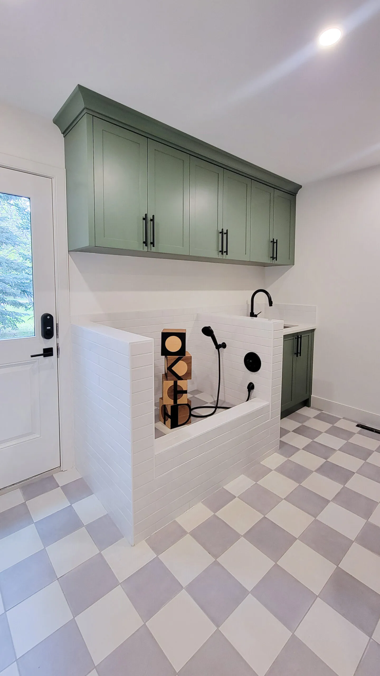 Image of doggy bath mud room with green millwork and checkered tile floors.