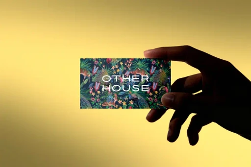 a hand holding a floral jungle inspired business card that reads Other House