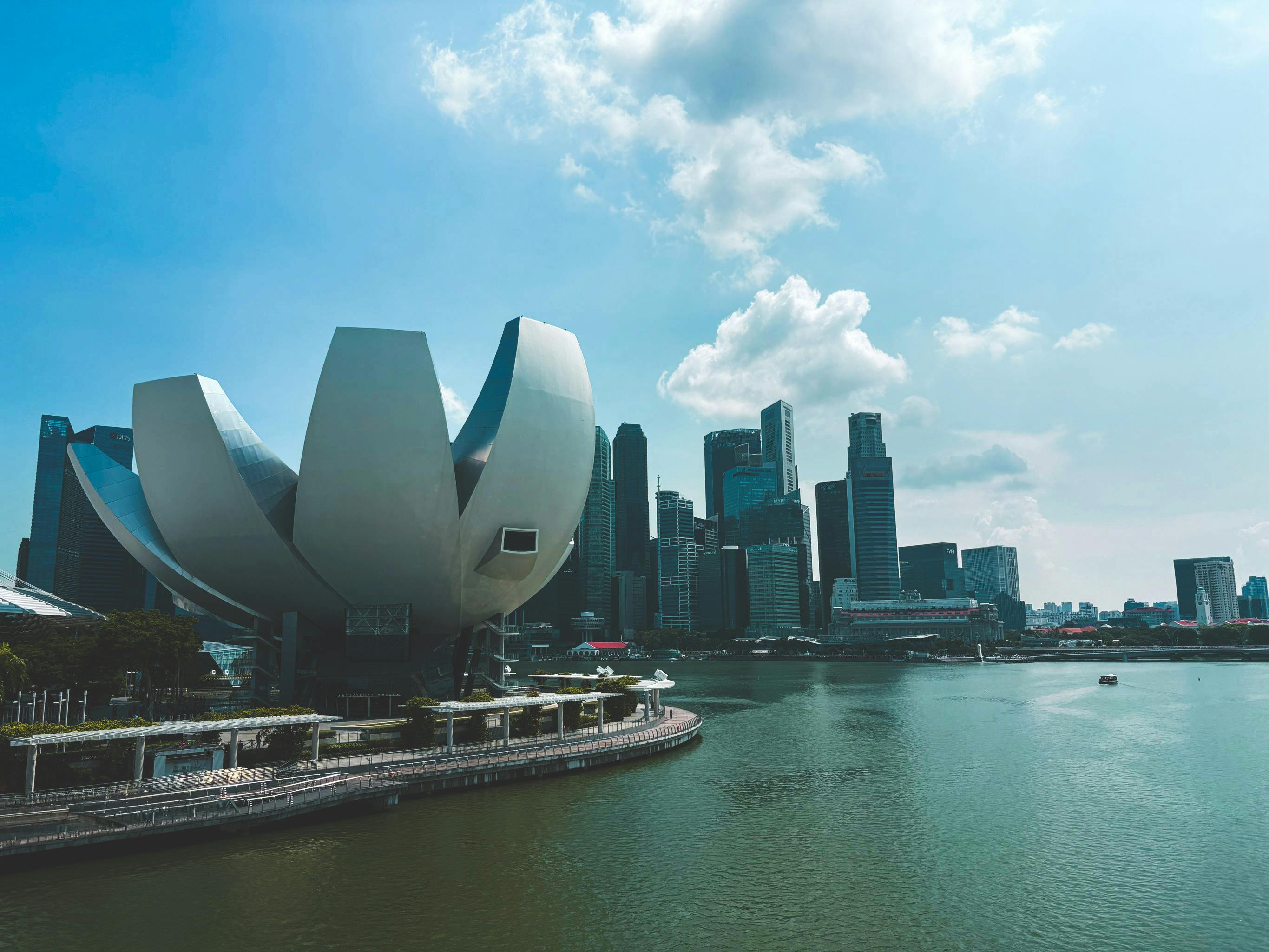 The ArtScience Museum, shaped like a white lotus flower, sits on the edge of Marina Bay. In the background, the modern skyscrapers of the central business district rise under a clear sky.