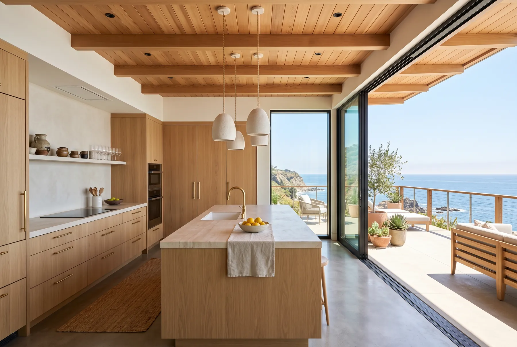 White oak kitchen with a stone island, open to an ocean-view terrace