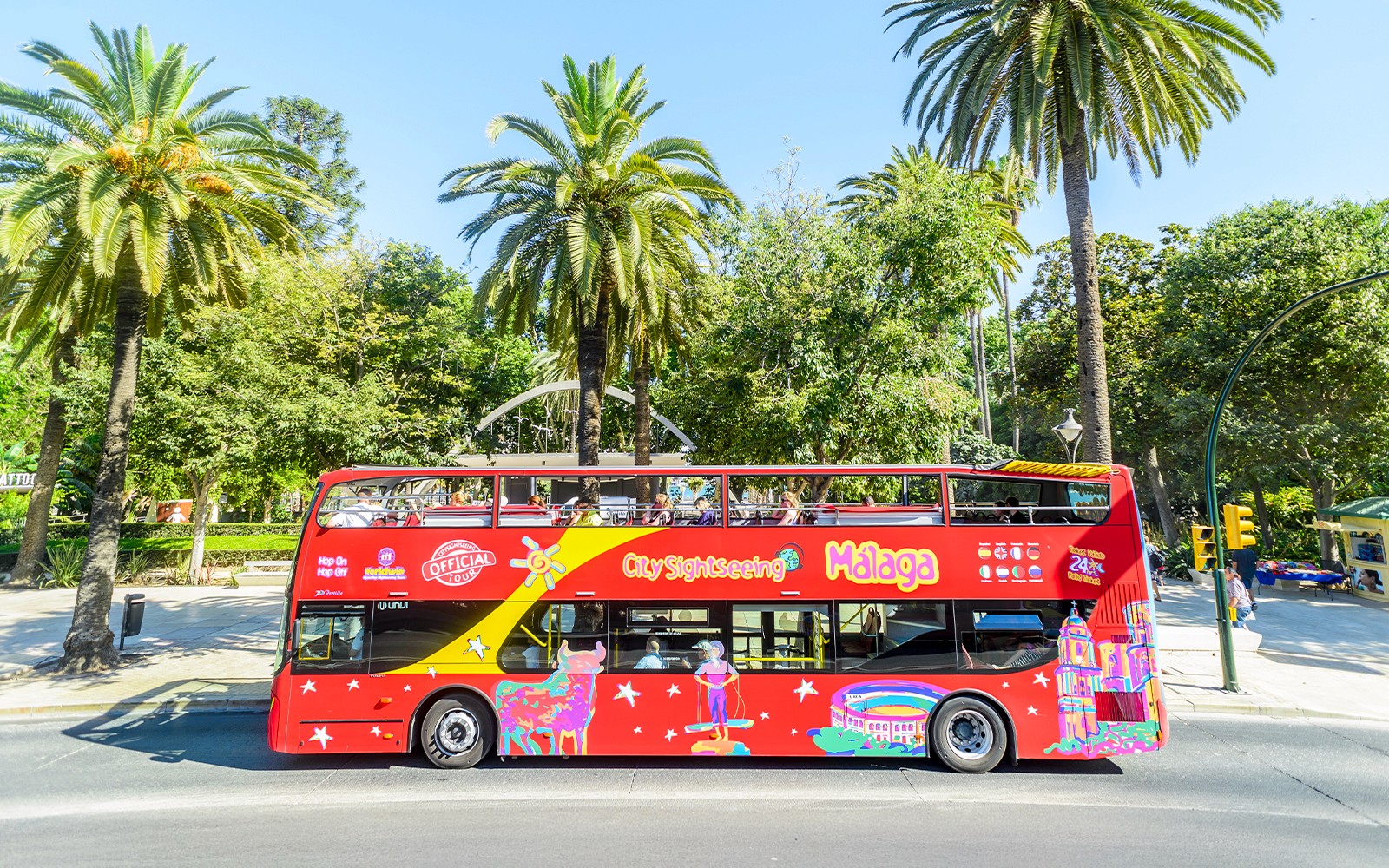 Red double-decker bus for Malaga hop-on hop-off tour near palm trees.
