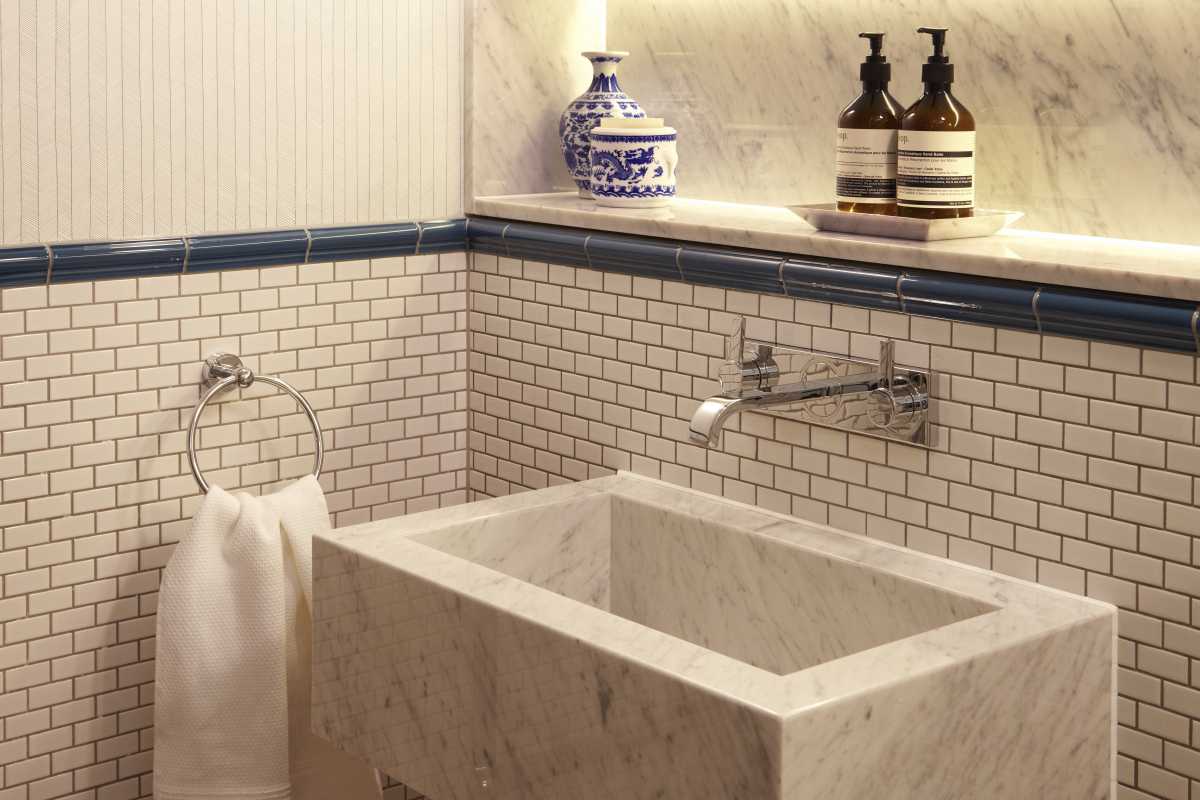 Elegant powder room styled by Doll & Co. Interior Designers in the City of London, showcasing a carved marble block sink, white subway tile wall, and polished chrome tapware.