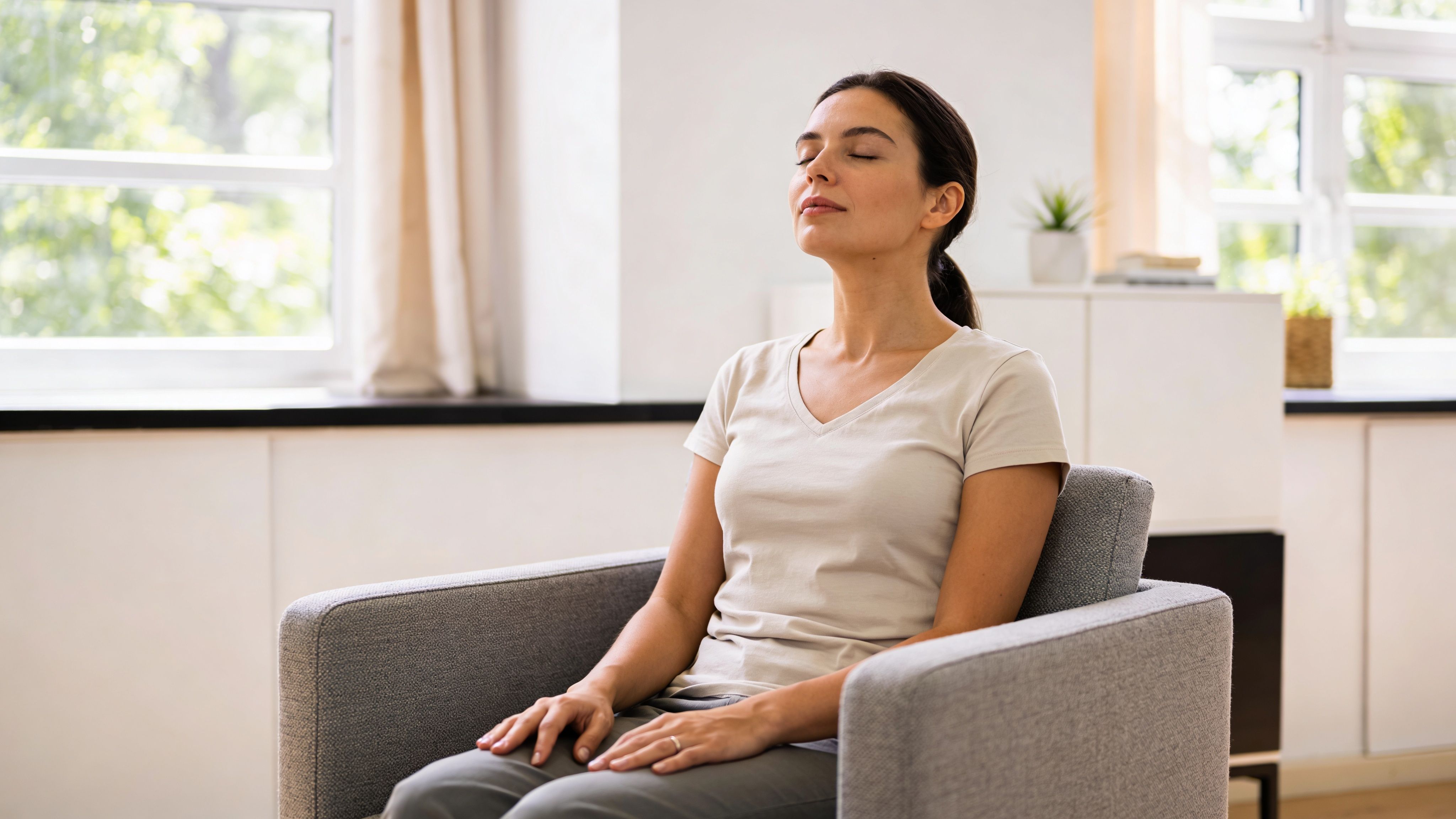 A young woman sitting in a comfortable armchair, practicing deep breathing or meditation to find inner peace.