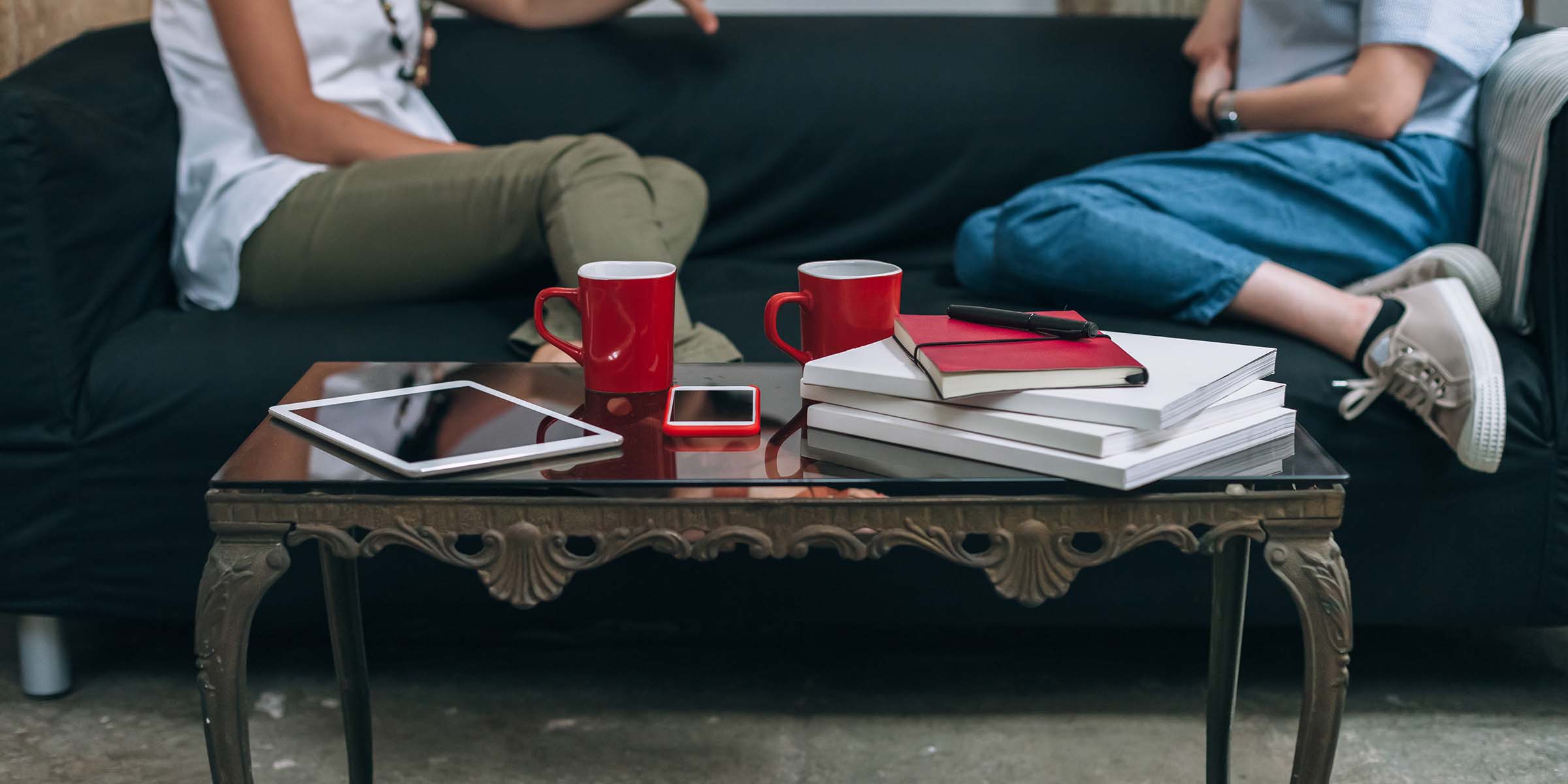 A glass and metal coffee table with notepads, coffee mugs and a phone on