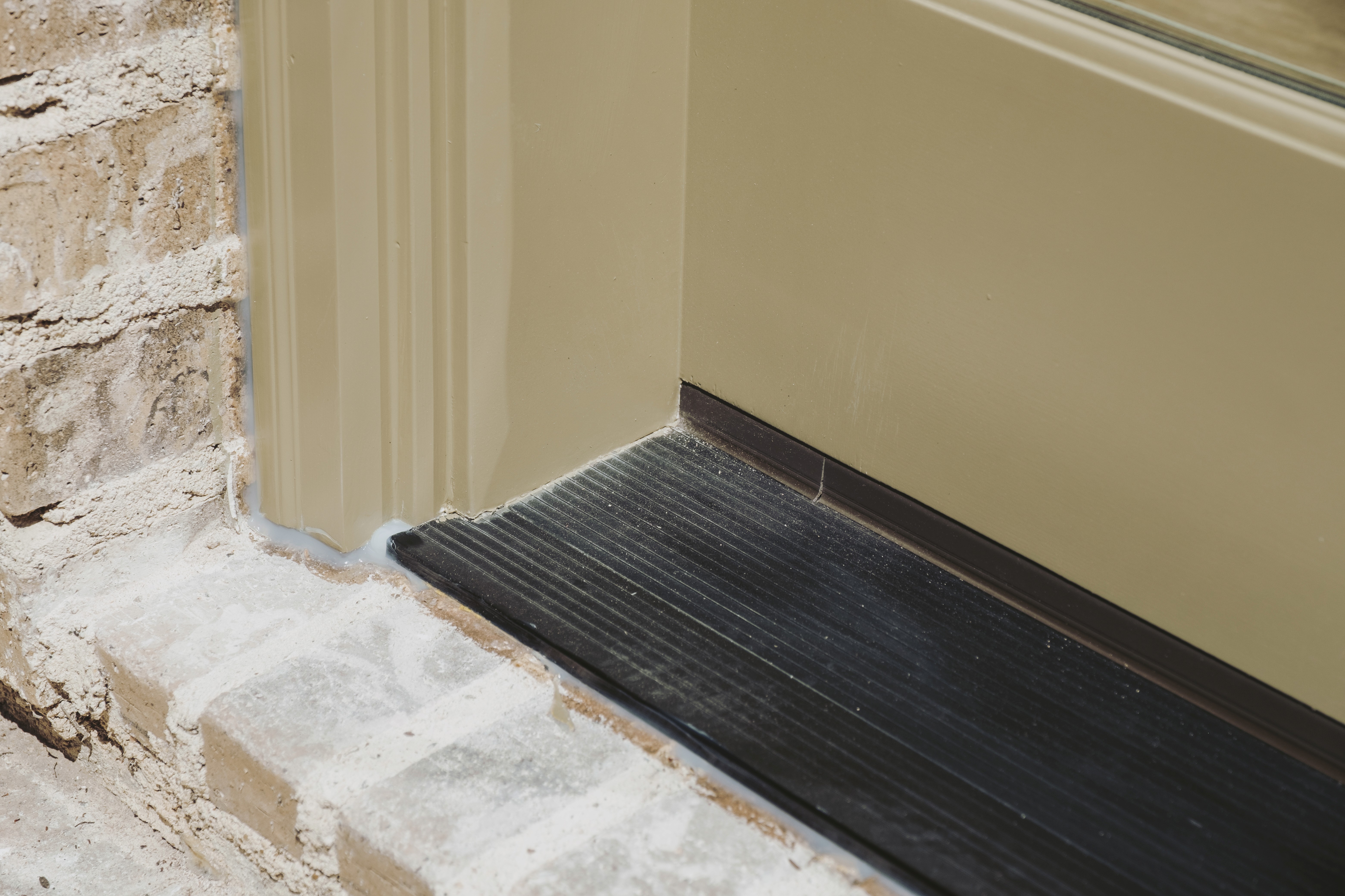 A close-up of professional door weatherproofing and sealing by Your New Door, featuring a properly installed black threshold and fresh caulking along a tan frame and brick exterior to prevent drafts, leaks, and energy loss.